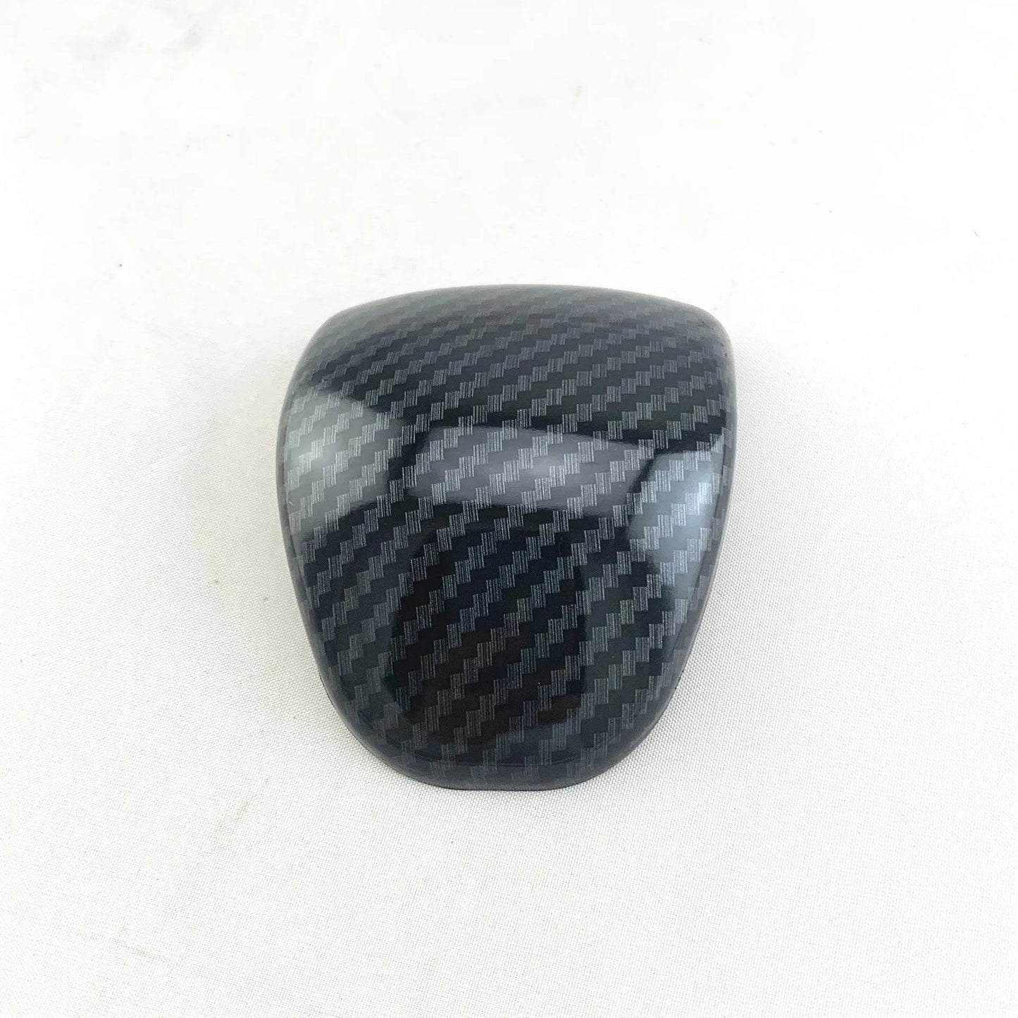 Black carbon fibre effect plastic cover for a car gear shift knob.