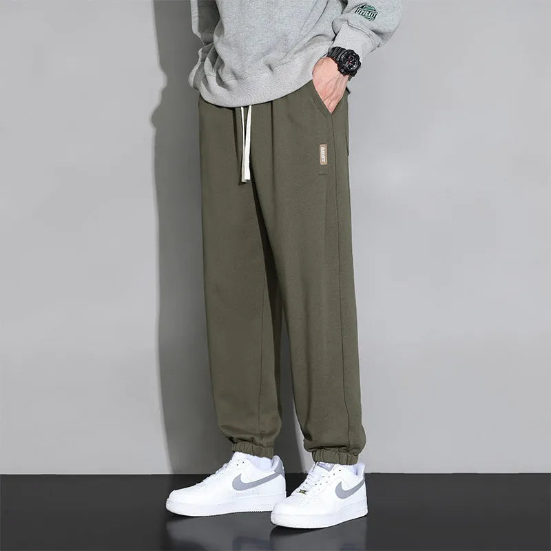 Man wearing loose grey sports trousers with an elasticated drawstring waistband.