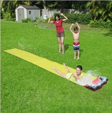 Children playing on a yellow inflatable water slide in a backyard garden