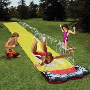 Children playing on a yellow inflatable water slide in a backyard garden