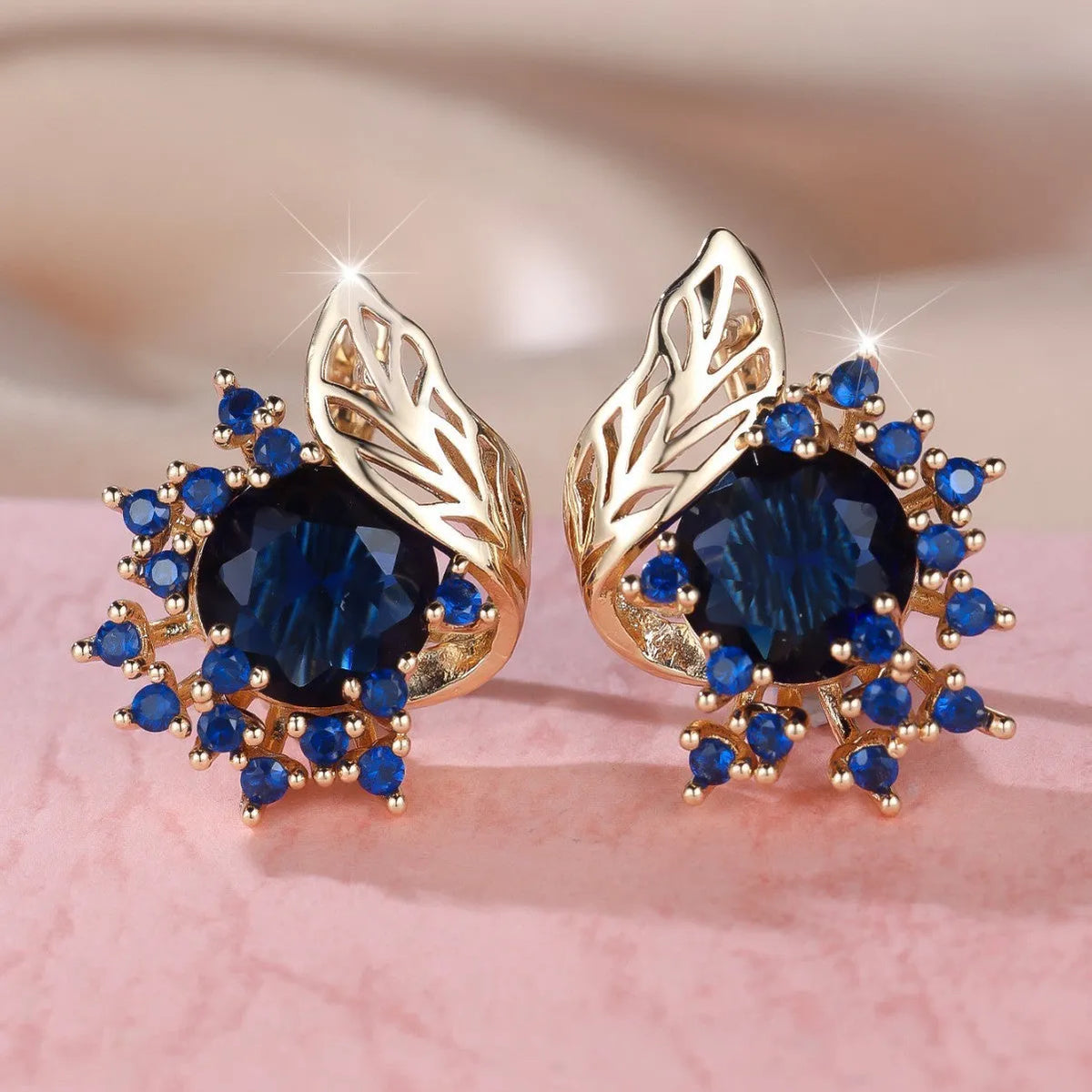 Rose gold plated women's stud earrings with a round flower shape, feather detail, and a central cubic zirconia stone.