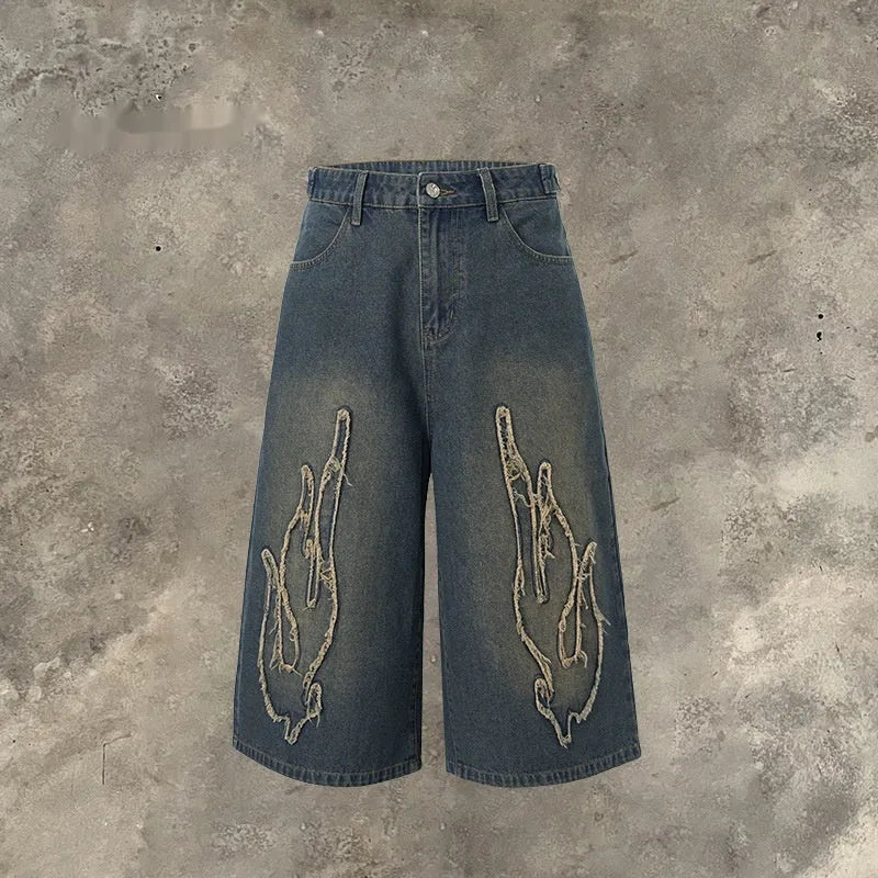 Men's black cropped denim shorts with a red and yellow flame embroidery patch on the leg.