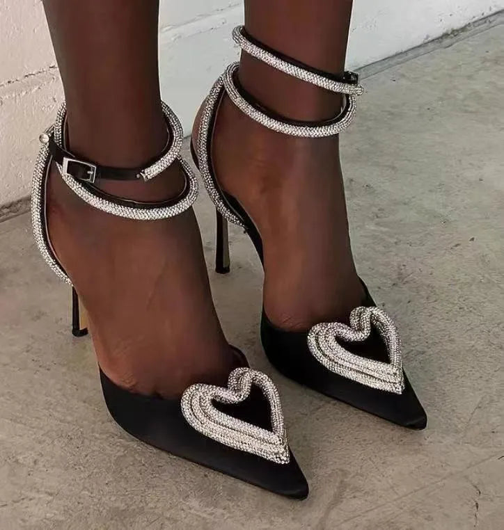 Women's pink satin sandals with heart-shaped rhinestone toe holders and adjustable cross straps on a white background.