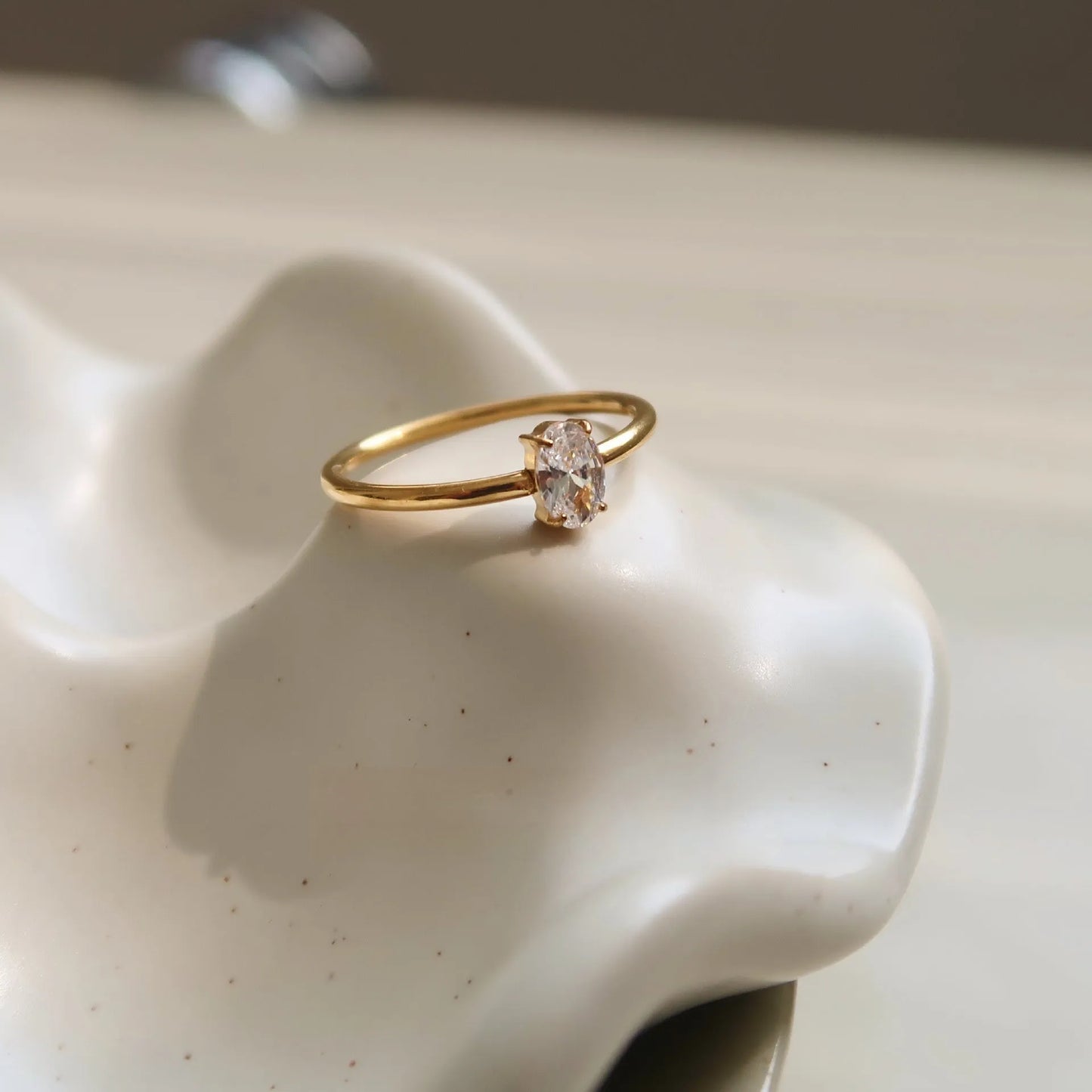 A gold-coloured stainless steel ring in a heart shape and an oval shape on a simple band.