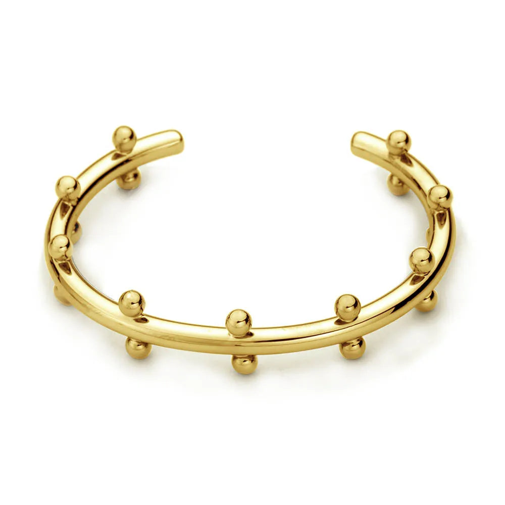 Close-up of a textured stainless steel C-shaped bracelet with rivet-shaped bean beads in a gold finish.