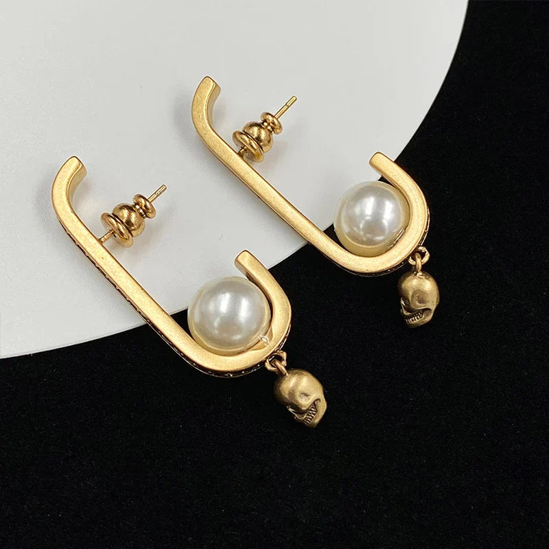 Pair of gold-tone earrings with a skull-shaped design, featuring pearls and diamonds