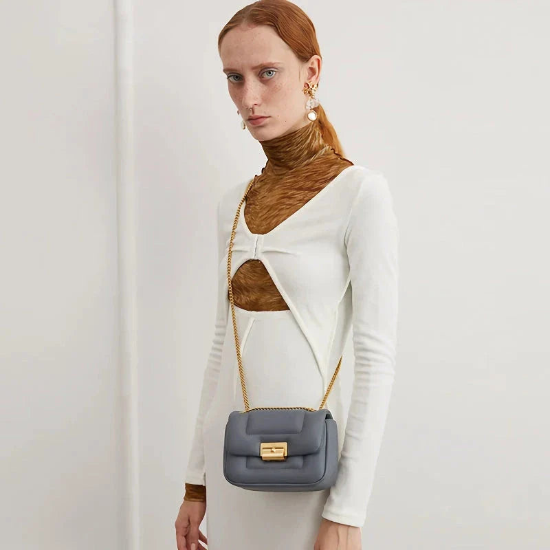 Grey leather crossbody bag with adjustable metal shoulder strap and secure hasp closure