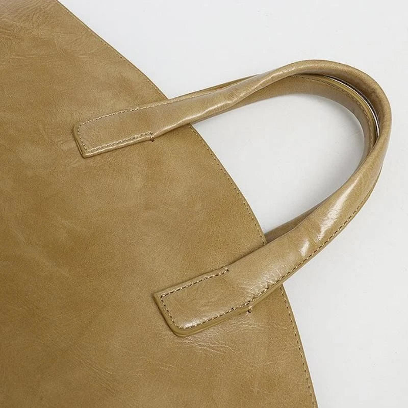 Elegant vegan leather tote bag with a unique bucket shape, short handles, and long straps for versatile carrying options