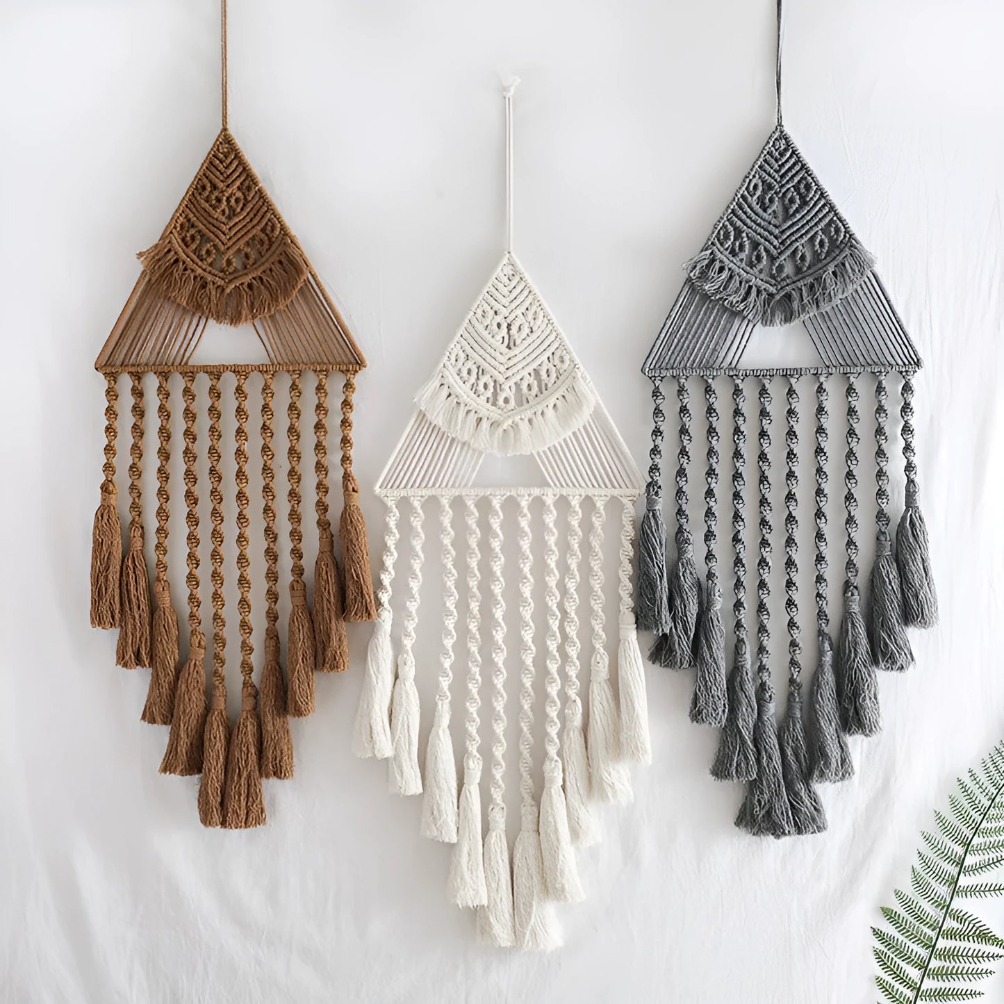 Large white handwoven triangle dream catcher pendant with wooden beads and a long tassel hanging on a wall.