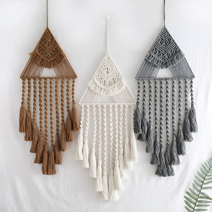 Large white handwoven triangle dream catcher pendant with wooden beads and a long tassel hanging on a wall.