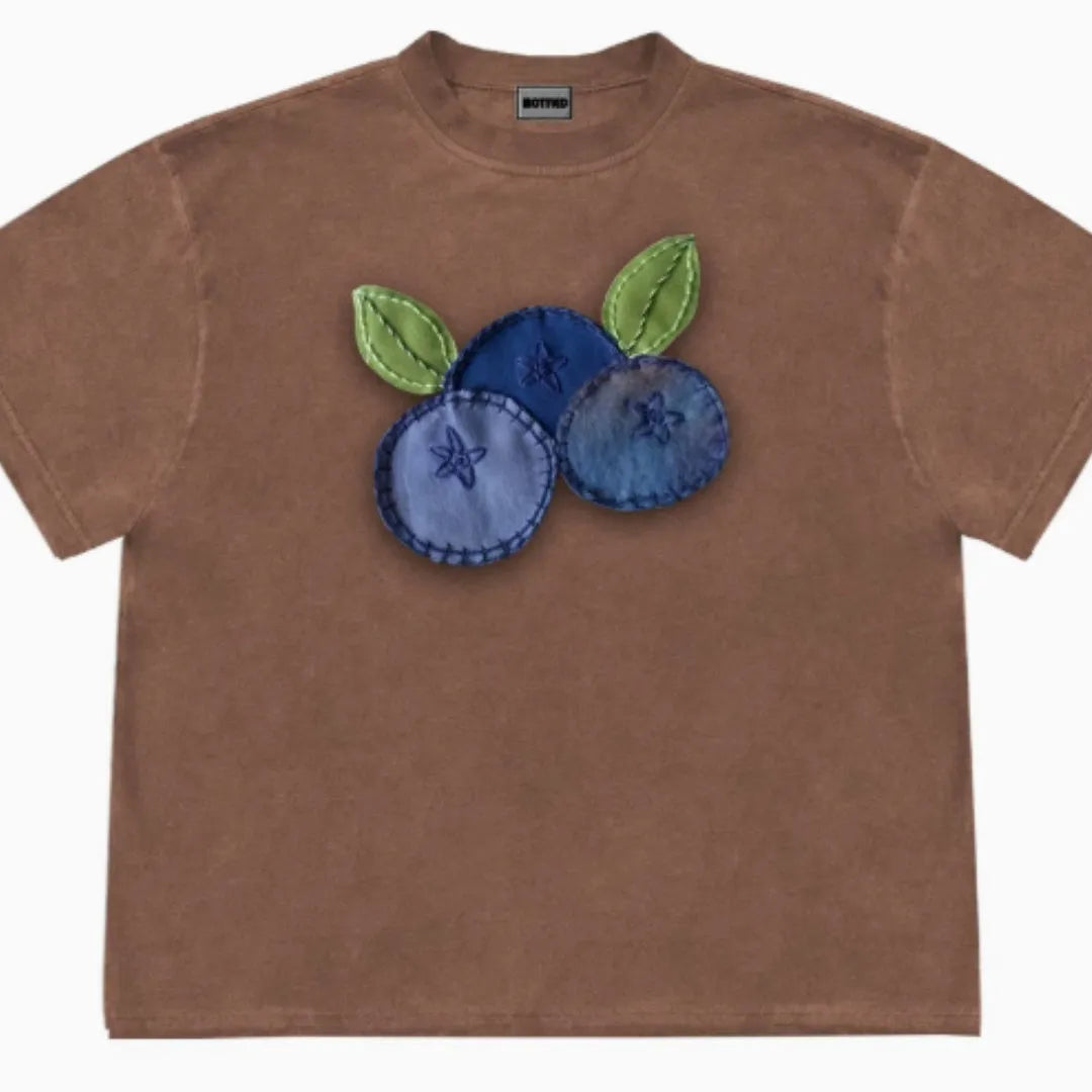 A loose-fit blueberry patchwork short-sleeve T-shirt on a hanger, showing plant and flower designs.
