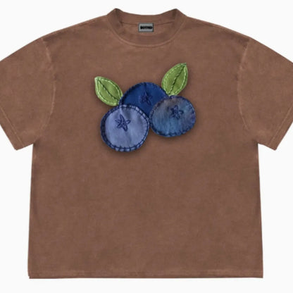 A loose-fit blueberry patchwork short-sleeve T-shirt on a hanger, showing plant and flower designs.