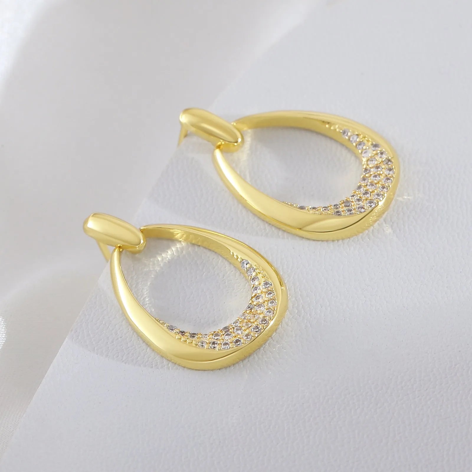 Women's yellow gold geometric drop earrings with oval and round elements on a white background.