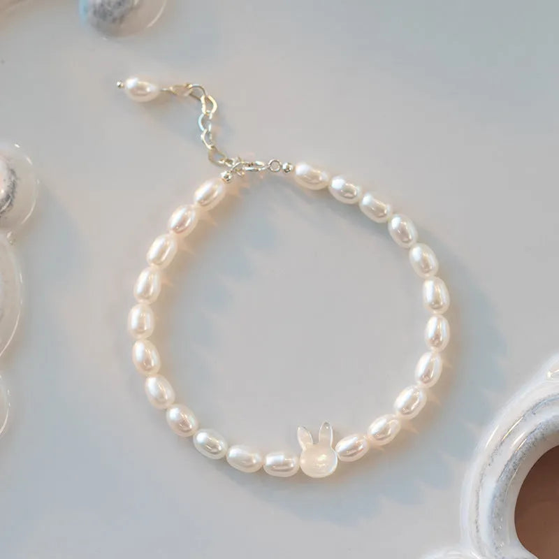 White pearl elastic bracelet with small rice-shaped beads and silver rabbit charm on wrist