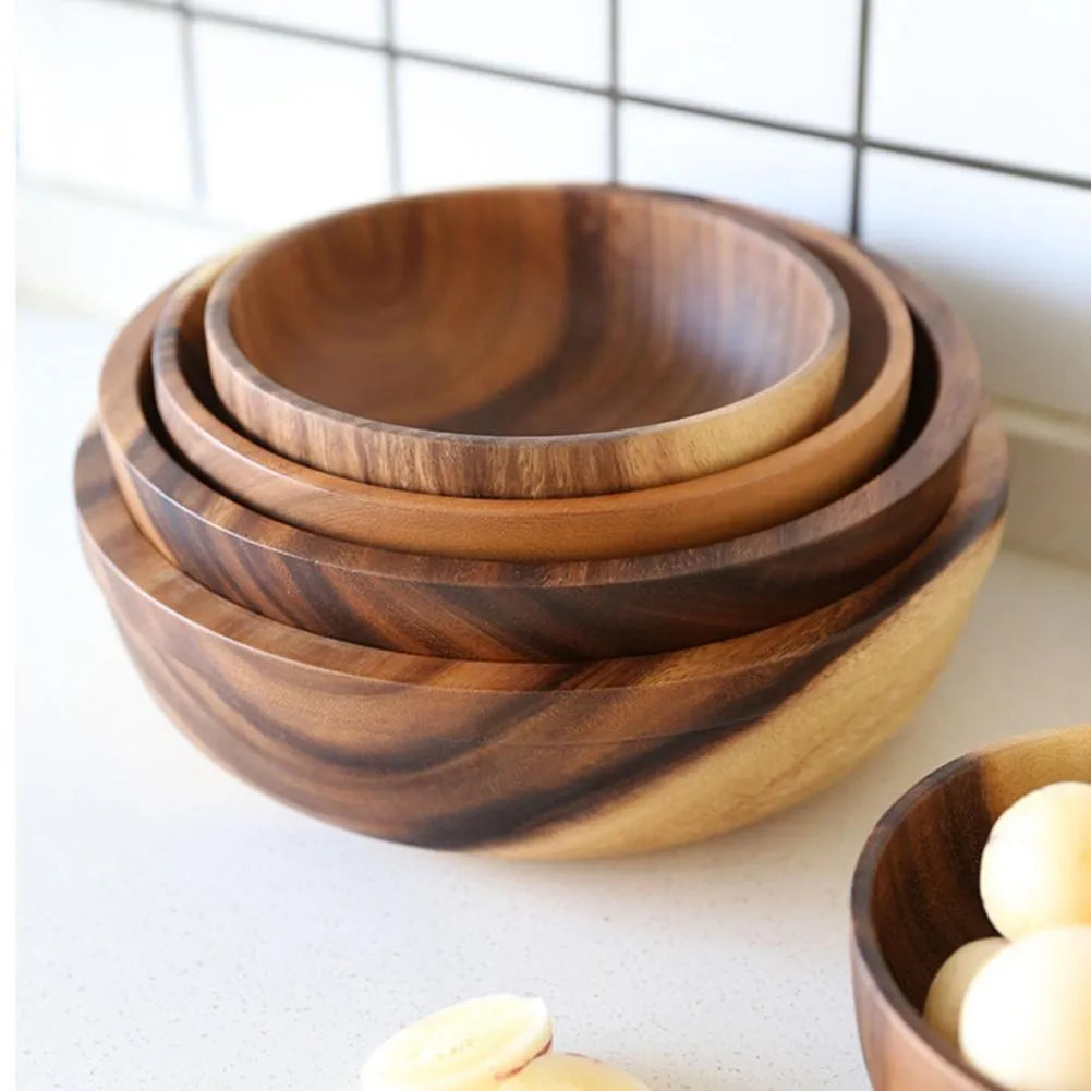 Set of five brown wooden bowls in different sizes on a wooden table, showing natural grain.
