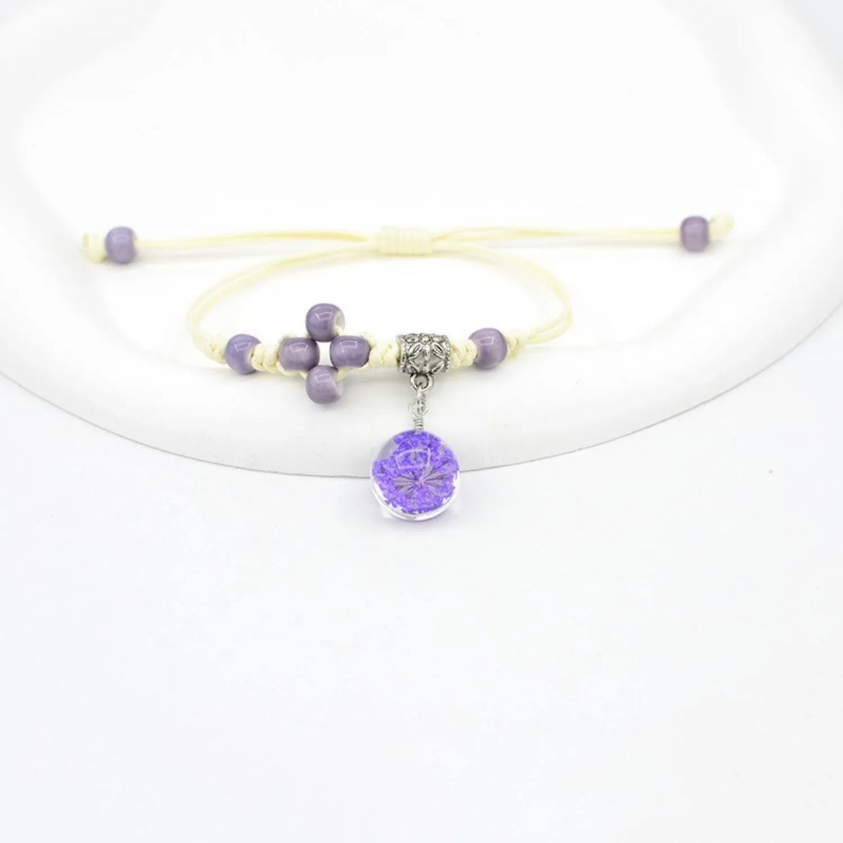 Close-up of a hand-woven bracelet with a large 1.4cm glass bead containing colourful dried flowers.