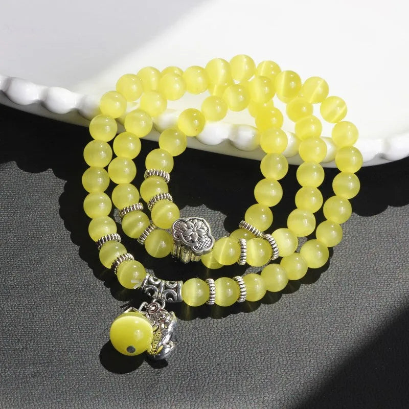 Close-up of a women's opal cat eye bracelet with three geometric rings and a lucky cat charm on a long, adjustable cord.