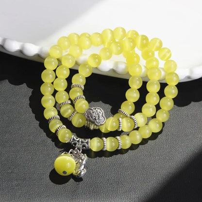 Close-up of a women's opal cat eye bracelet with three geometric rings and a lucky cat charm on a long, adjustable cord.