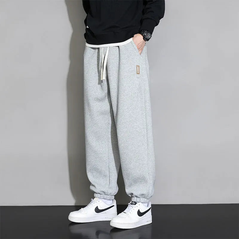 Man wearing loose grey sports trousers with an elasticated drawstring waistband.