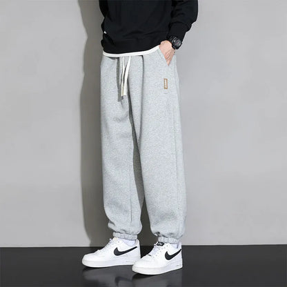 Man wearing loose grey sports trousers with an elasticated drawstring waistband.