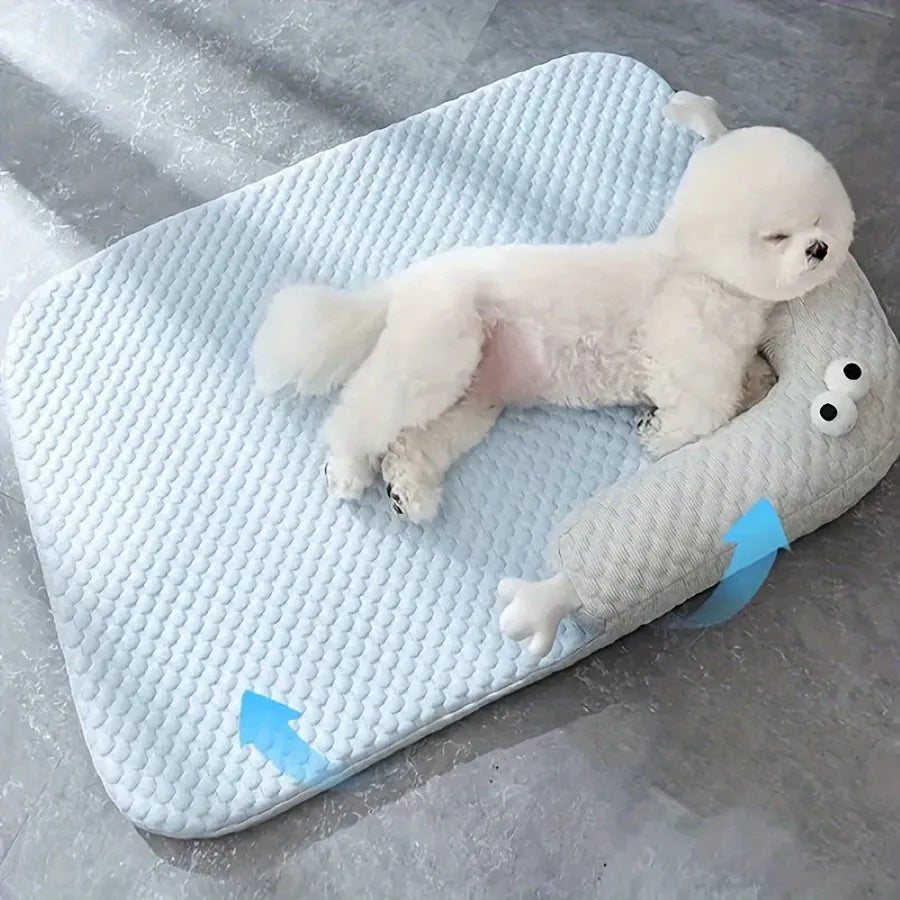Blue pet bed cushion with big-eyed monster design, shown on a wooden floor.