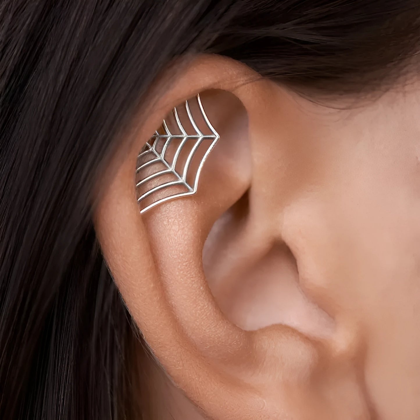 Close-up of a geometric spider web design on a gold-toned metal stud earring.