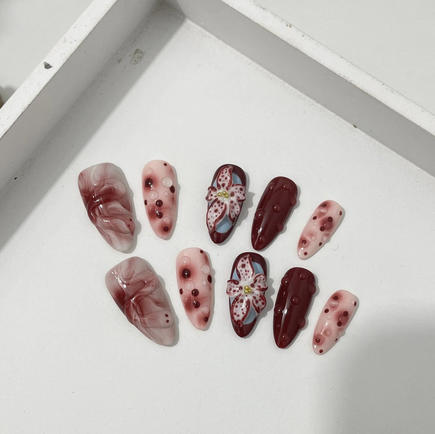 Hand-painted 3D carved nail wraps in Almond colour showing floral and geometric designs for mid-length manicures.