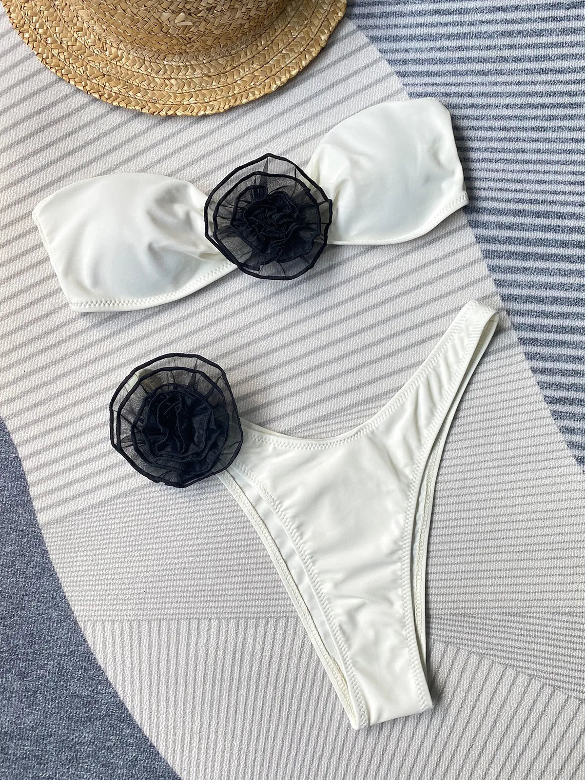 Black bikini with cross-back tube top, 3D white flower on bust, and high-leg split briefs on a model.