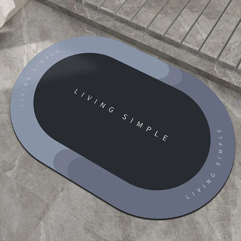Oval grey bath mat with non-slip rubber bottom on a tiled floor, showing absorbent fabric surface