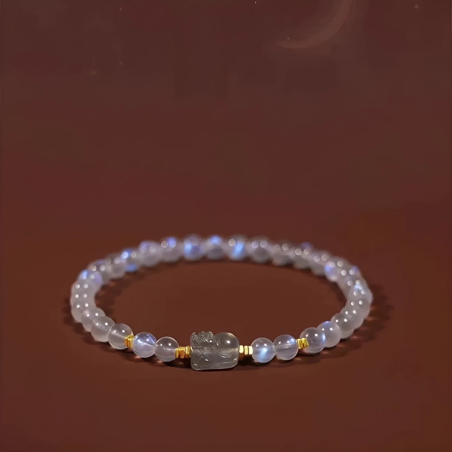 Close-up of a women's moonstone bracelet with an animal or Zodiac motif on a blue background.