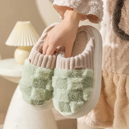 Plaid pattern women's plush slippers with coral velvet upper and textured PVC sole on a wooden floor.