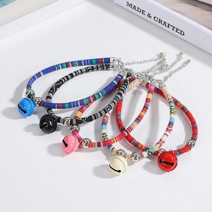 Coloured ethnic pattern adjustable dog collar with metal bell and reflective strip on a nylon strap.