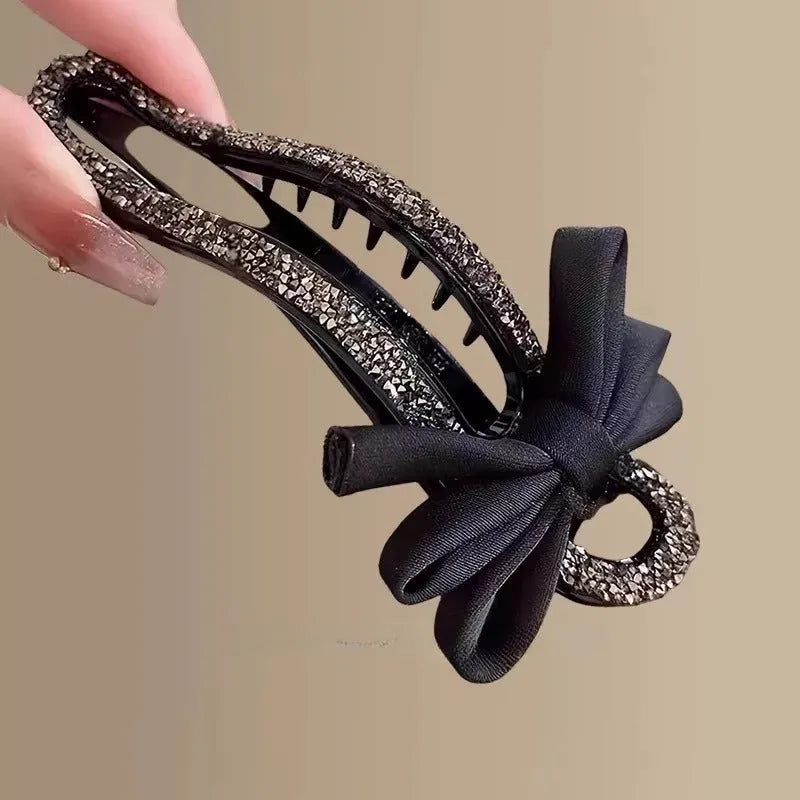 A black crystal bow on a clear 11.5cm long acrylic banana hair clip with bobby pin back.