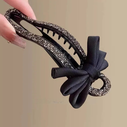 A black crystal bow on a clear 11.5cm long acrylic banana hair clip with bobby pin back.