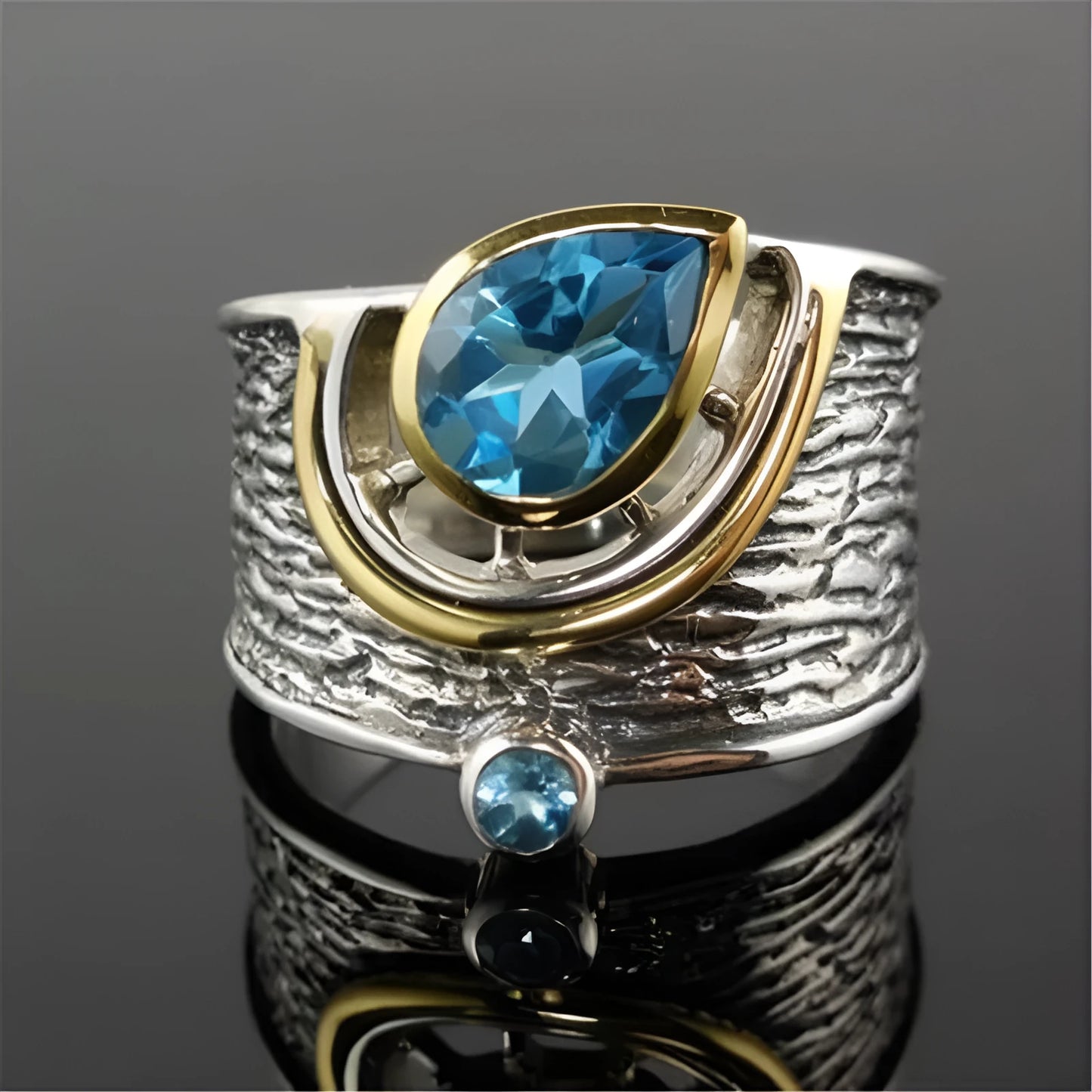 Close-up of a women's blue zircon ring with a teardrop-shaped stone inlaid in an alloy band, shown on a finger.