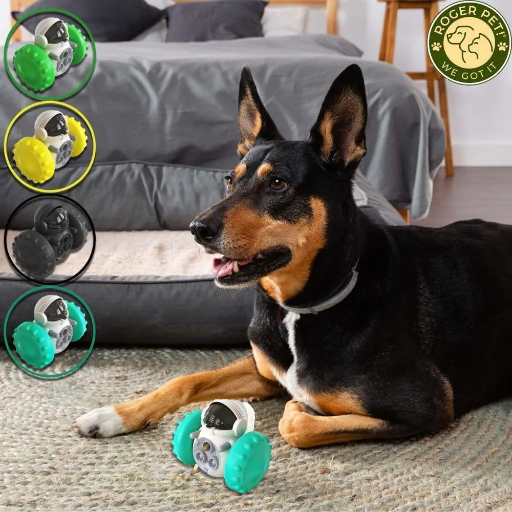 A black, robot-shaped treat dispenser toy for dogs and cats on a wooden floor, showing its size and rolling design.
