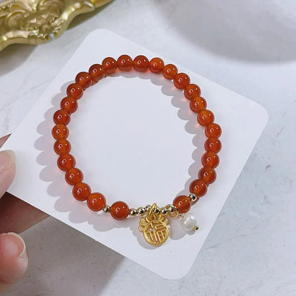 Close-up of a red agate bracelet with a dragon charm and Lucky Bag symbol on a wrist.