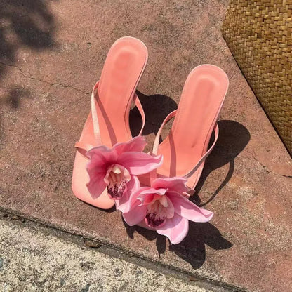 Pink women's sandals with a satin upper, artificial white Phalaenopsis flower, square toe, and a mid-height heel.