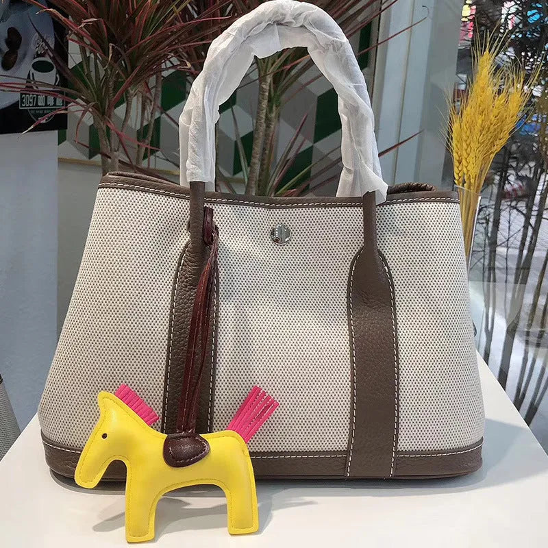 Canvas and leather tote bag in bucket shape with crossbody strap, shown in black, brown, gray or red colour options