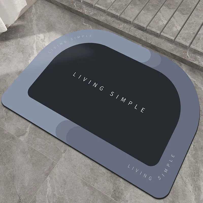 Oval grey bath mat with non-slip rubber bottom on a tiled floor, showing absorbent fabric surface