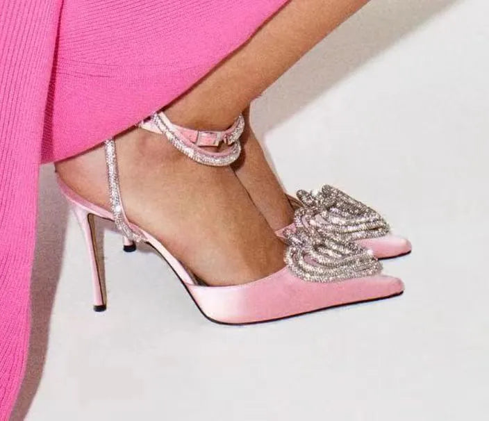 Women's pink satin sandals with heart-shaped rhinestone toe holders and adjustable cross straps on a white background.