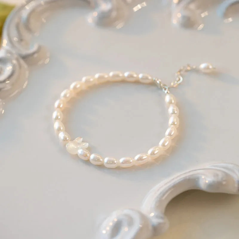 White pearl elastic bracelet with small rice-shaped beads and silver rabbit charm on wrist