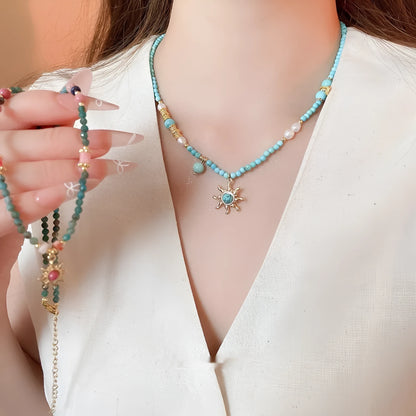 Geometric sun stone pendant on a freshwater pearl necklace with gold and blue electroplated finish.