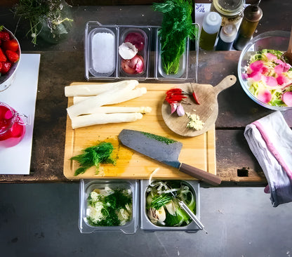 Bamboo cutting board with smooth surface alongside two large and three small plastic storage trays for vegetables and meat.