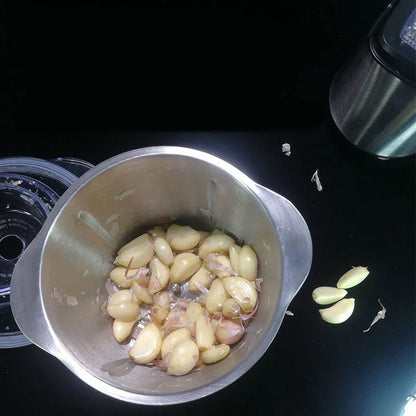 White electric garlic peeler appliance with stainless steel bowl and clear plastic lid on a kitchen counter.