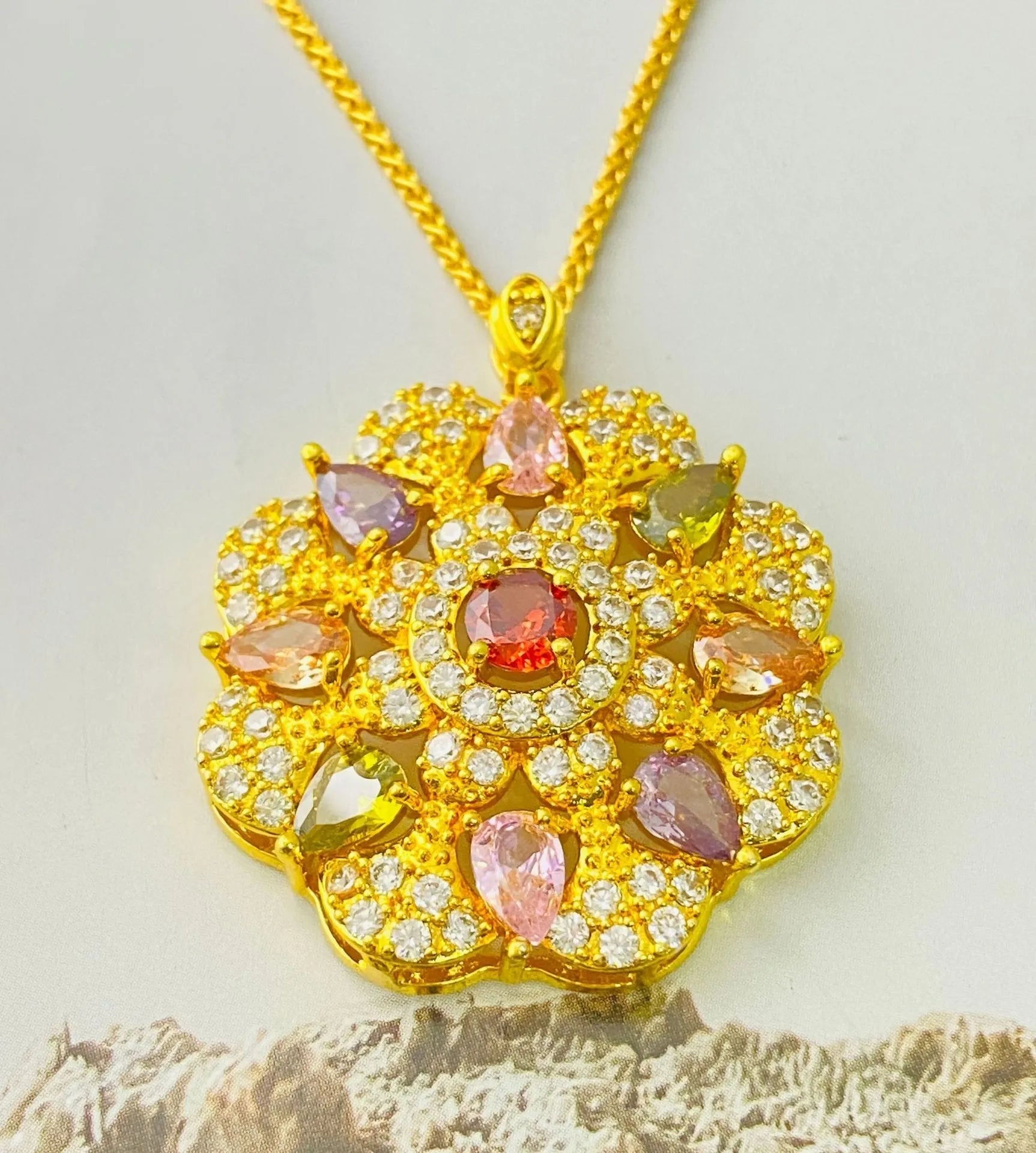 Close-up of a women's flower-shaped pendant necklace with a colourful zircon stone in a choice of gold, champagne gold, or platinum colour finishes.