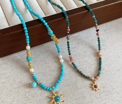Geometric sun stone pendant on a freshwater pearl necklace with gold and blue electroplated finish.