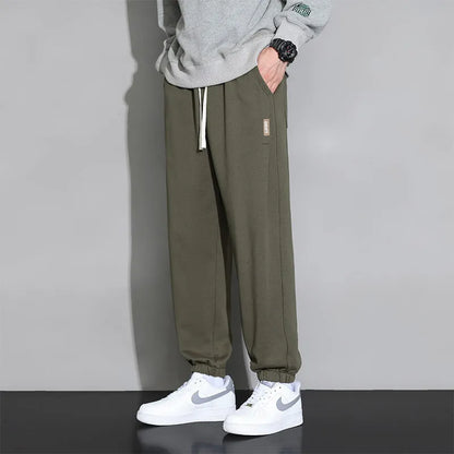 Man wearing loose grey sports trousers with an elasticated drawstring waistband.