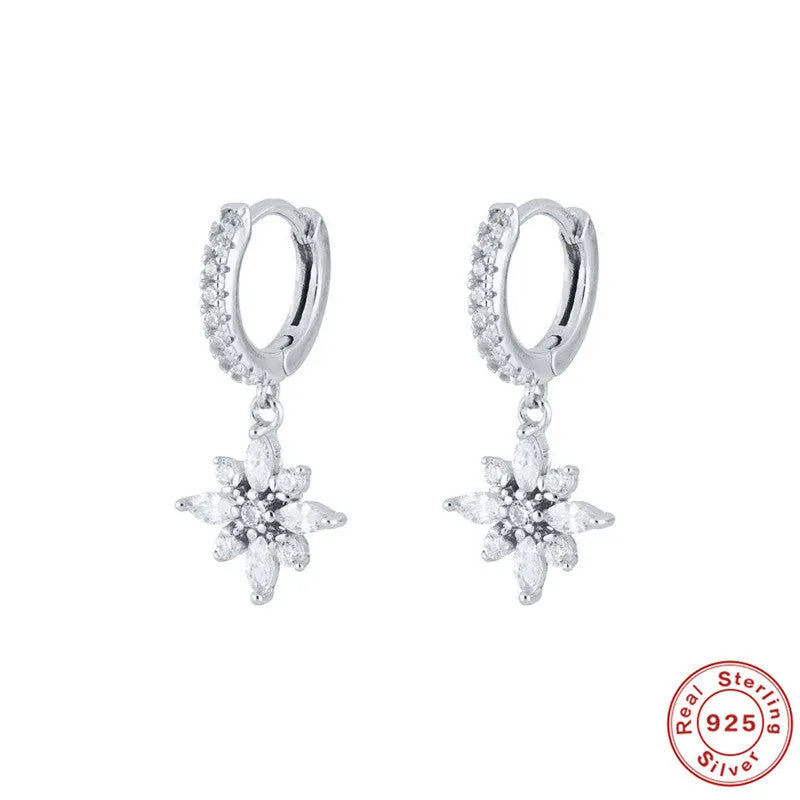 A pair of geometric snowflake pendant earrings in sterling silver with cubic zirconia stones, on a white background.