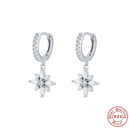 A pair of geometric snowflake pendant earrings in sterling silver with cubic zirconia stones, on a white background.